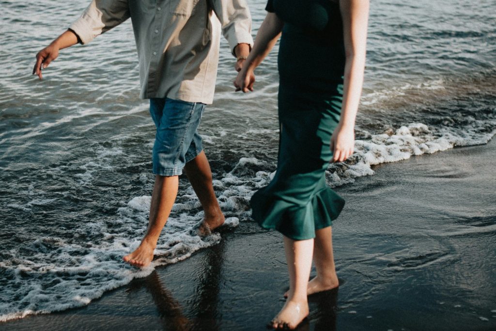 A couple holding hands and walking barefoot along the shoreline, enjoying a romantic beach moment together.