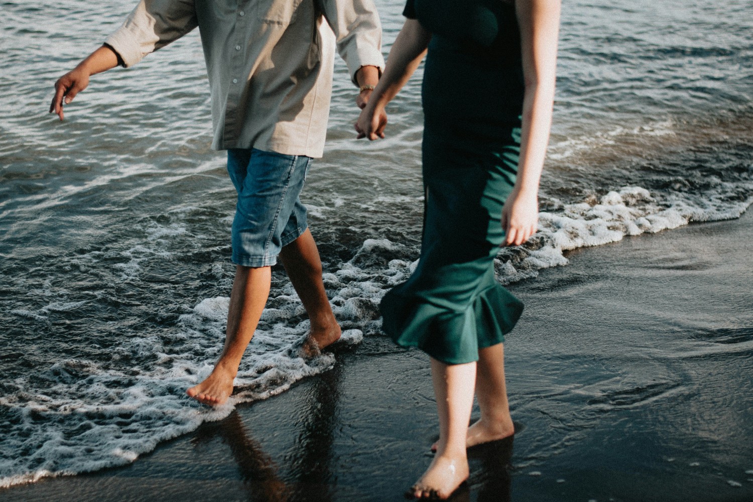A couple holding hands and walking barefoot along the shoreline, enjoying a romantic beach moment together.