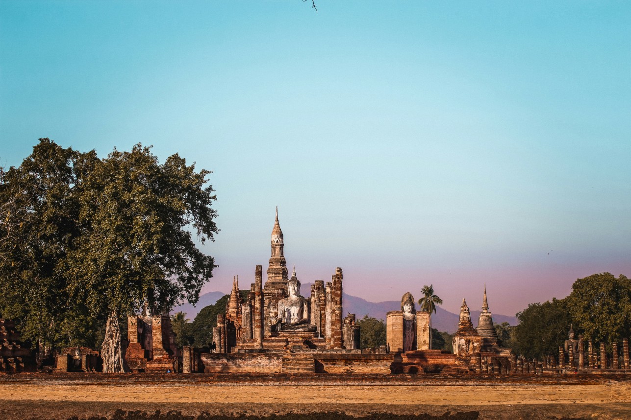 Buddha statue framed by crumbling stone pillars in Sukhothai.