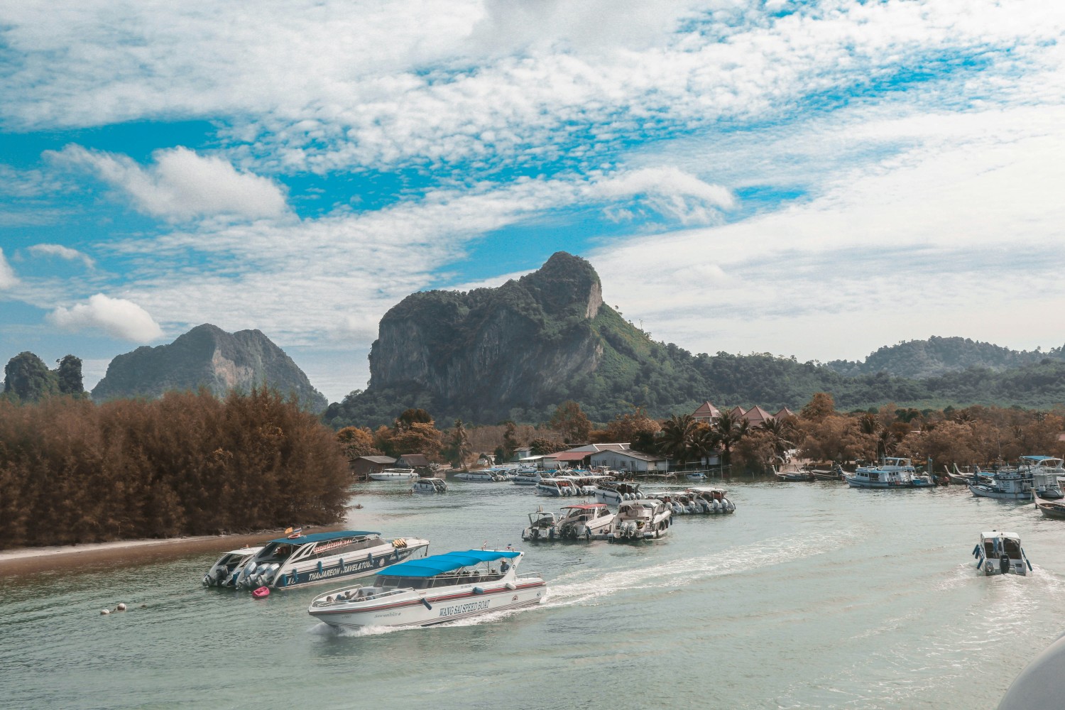 Scenic view of speedboats on the turquoise waters of Krabi, Thailand, with dramatic limestone cliffs and lush tropical greenery in the background under a partly cloudy blue sky