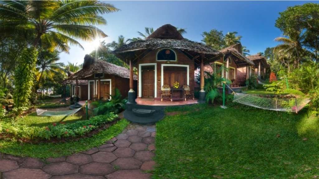 Traditional Kerala-style cottages surrounded by lush greenery and palm trees at Somatheeram Ayurveda Village in Kovalam, perfect for a peaceful Ayurvedic retreat.