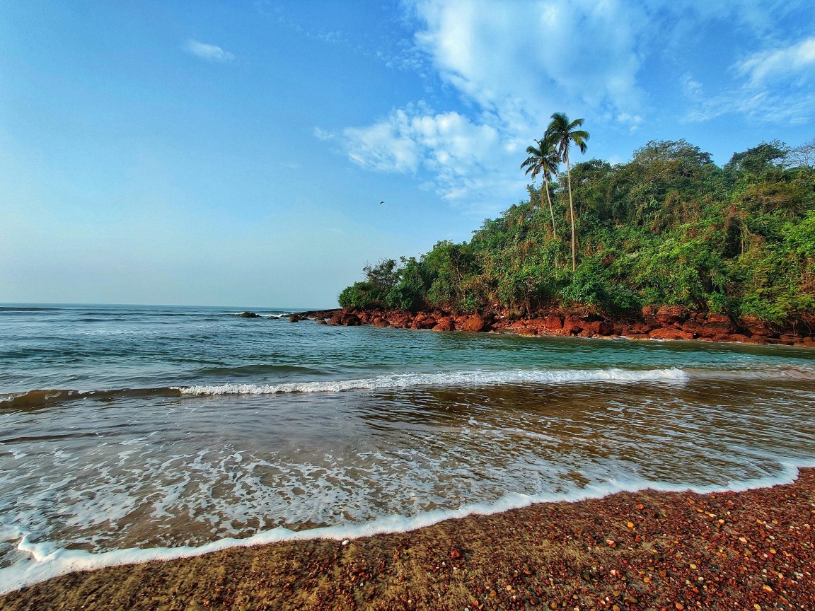 Azure waves crashing gently along a pristine Kerala coastline under a clear blue sky.