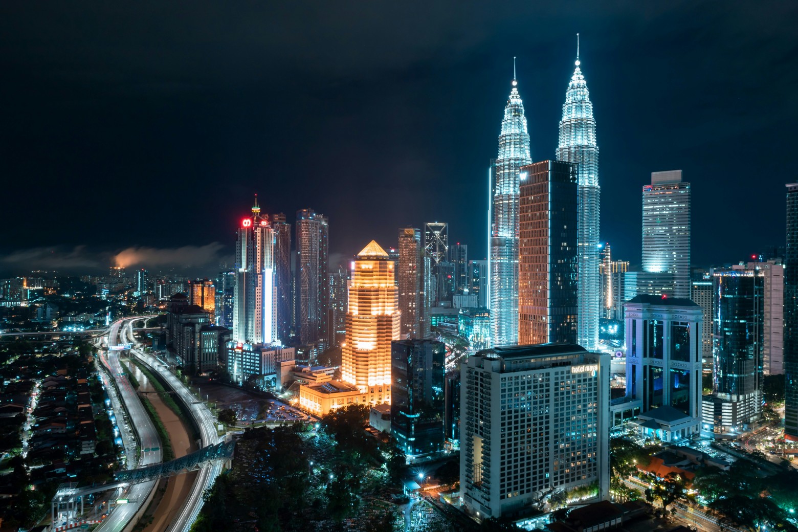 Night view of Kuala Lumpur skyline featuring the illuminated Petronas Twin Towers and surrounding skycrapers.