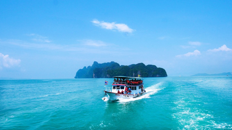 Speedboat cruising over clear turquoise waters near a tropical Island in Thailand under a bright blue sky.