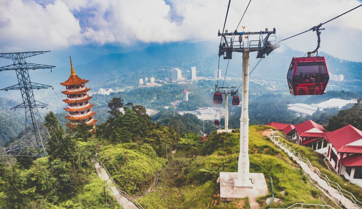 Scenic cable car ride overlooking lush green hills and a pagoda tower in Langkawi, Malaysia with city skyline in the background.