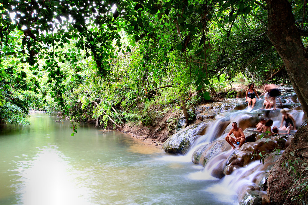 People relaxing in a natural hot spring waterfall surrounded by lush green jungle.