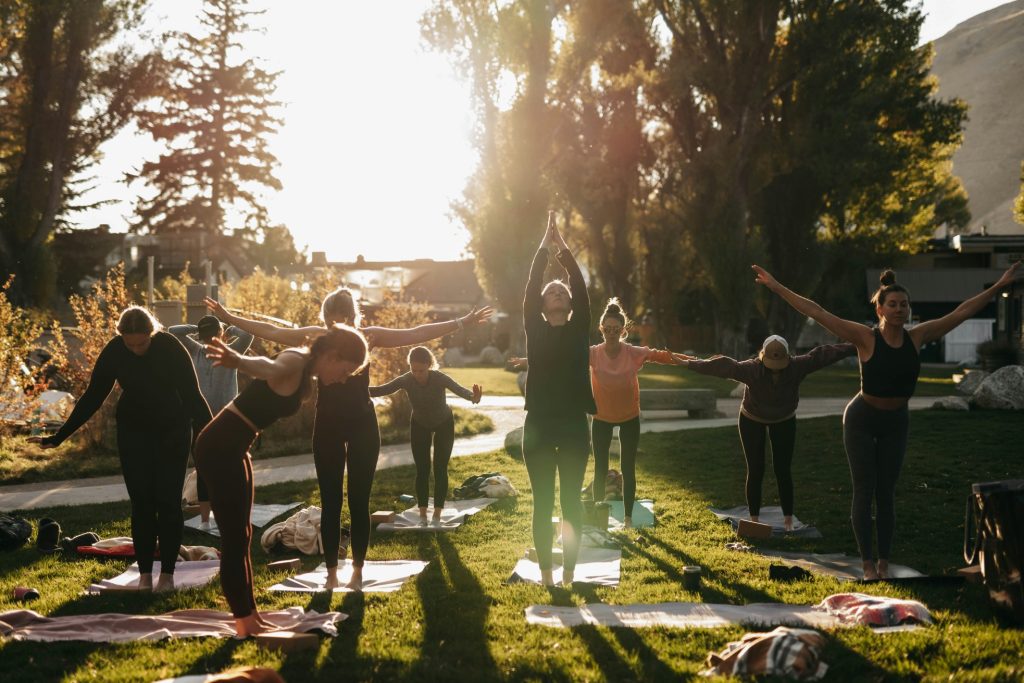 Group of people practicing yoga outdoors on a grassy field at sunset.