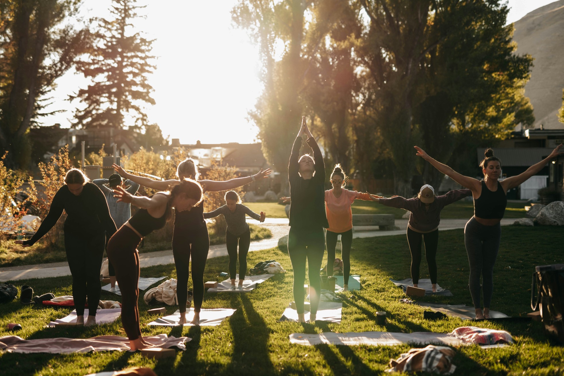 Group of people practicing yoga outdoors on a grassy field at sunset.